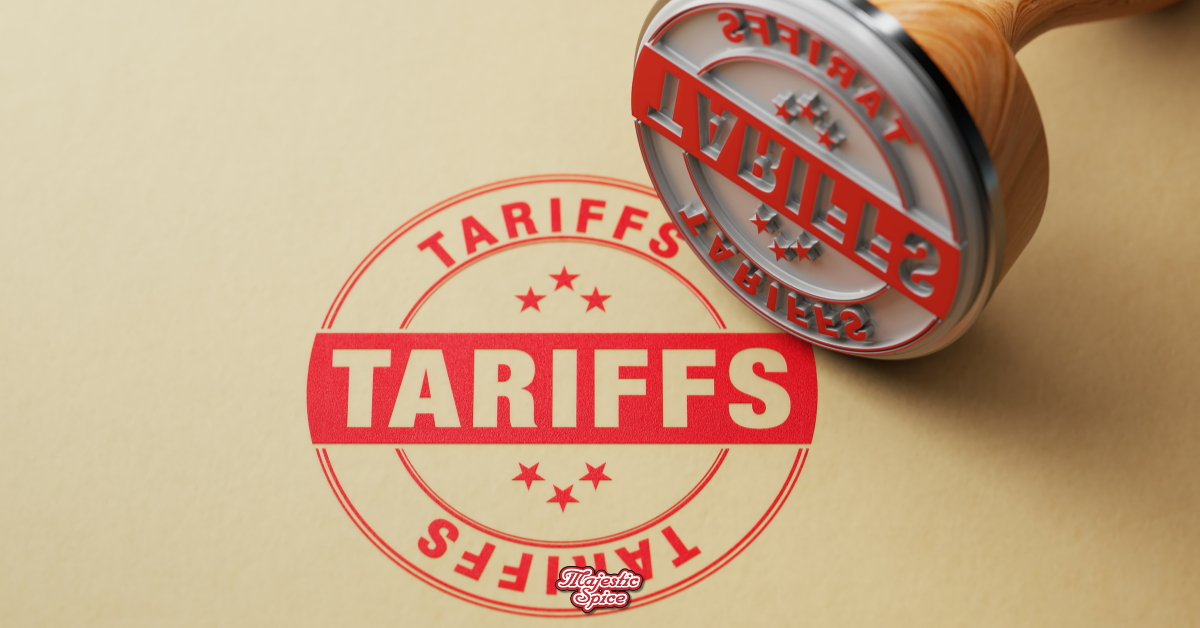 A rubber stamp with the word "TARIFFS" in bold red letters is pressed onto a beige document, leaving a clear red ink imprint. The design includes stars surrounding the text, giving it an official look. The "Majestic Spice" logo appears at the bottom of the image.