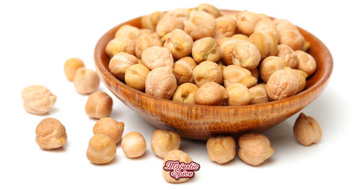 Wooden bowl filled with dried chickpeas, with some scattered on a white surface, Majestic Spice logo at the bottom.