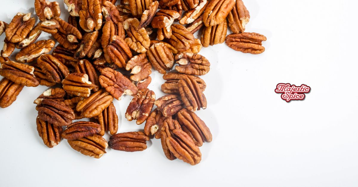 A pile of shelled pecan halves scattered on a white background with the Majestic Spice logo in red on the right side.