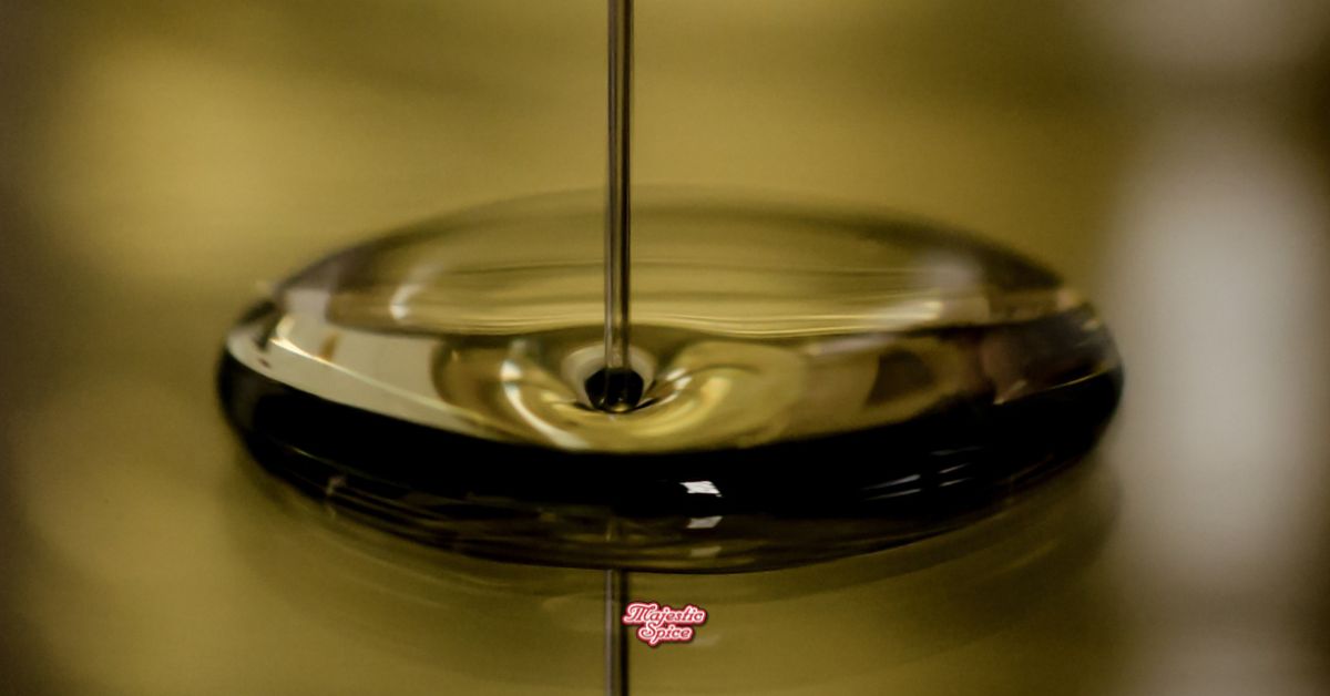 Macro shot of edible oil stream forming a glossy pool and ripple on a warm, blurred background; Majestic Spice watermark.
