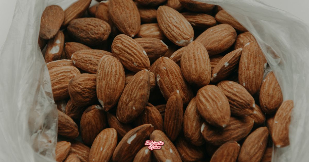 Close-up of whole raw almonds in a bulk poly bag. Small Majestic Spice logo in the bottom center.