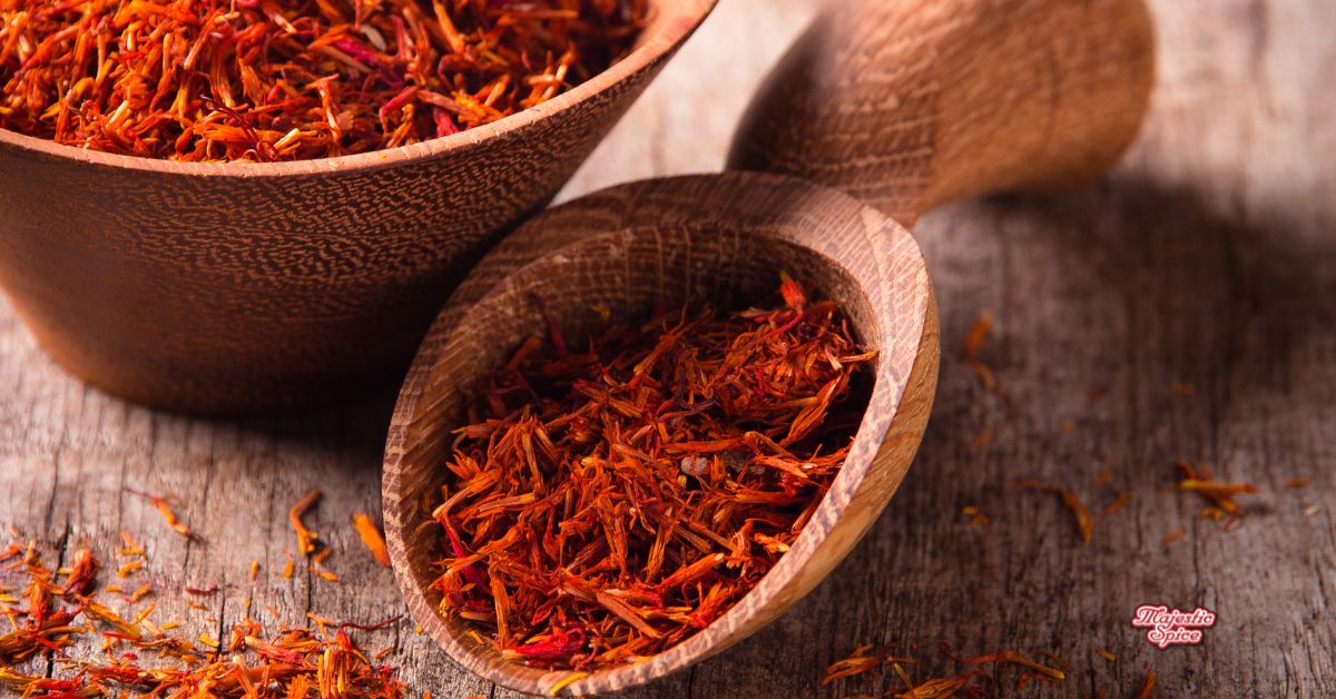 Saffron threads in a wooden bowl and scoop on a rustic table, Majestic Spice logo in the corner.