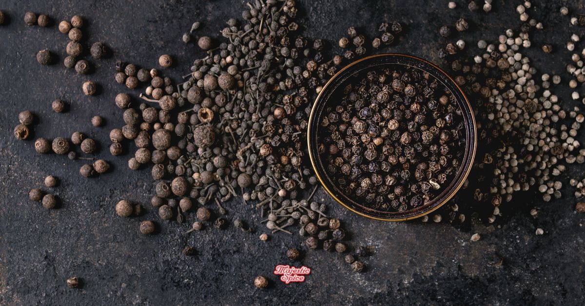 Bowl of black peppercorns with mixed pepper and spices scattered on a dark surface, Majestic Spice logo at the bottom.