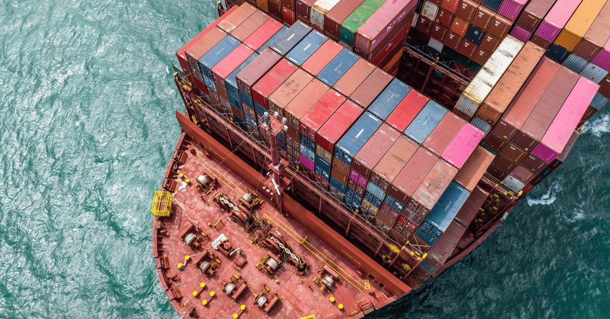 Aerial view of a large cargo ship loaded with colorful shipping containers navigating through the sea, representing global trade and export activity across major shipping routes.